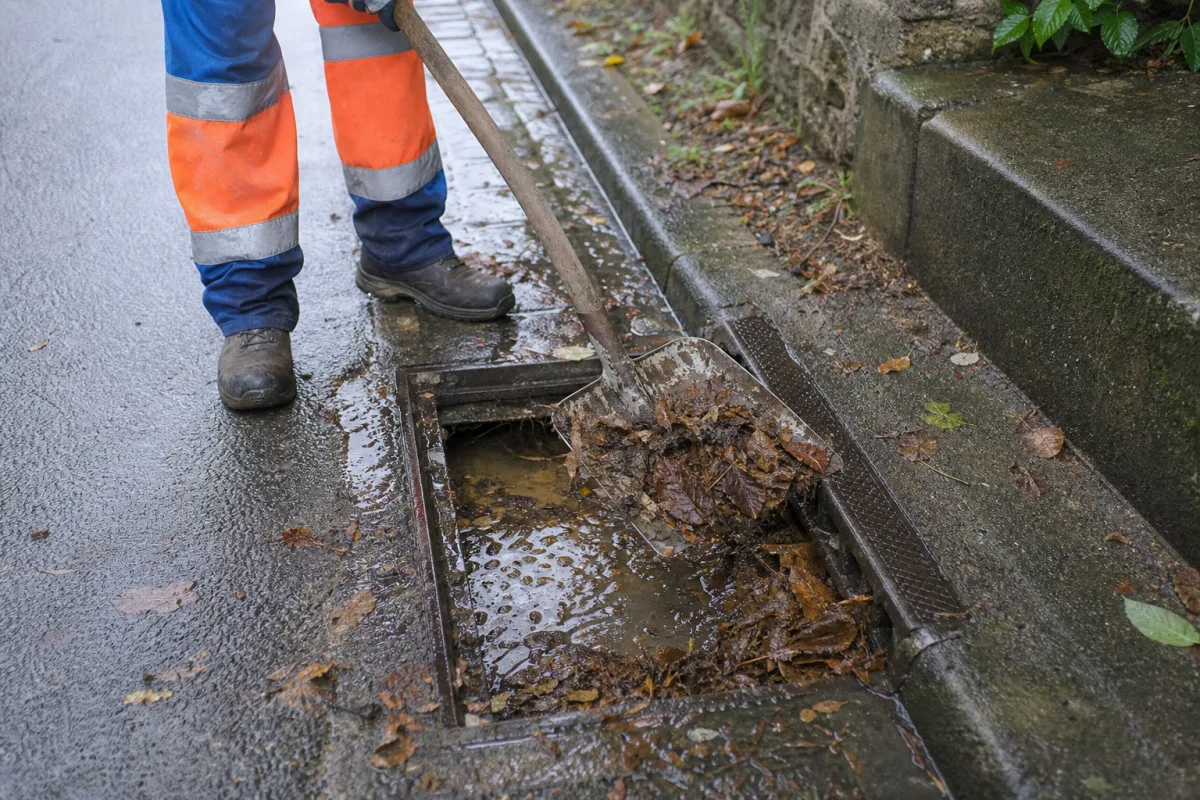Agent de voirie nettoyant un avaloir bouché d’eau stagnante